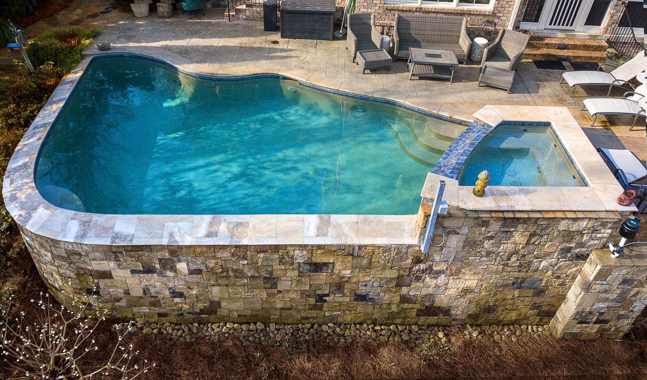 Freeform pool and spa with natural stone wall and travertine coping close-up