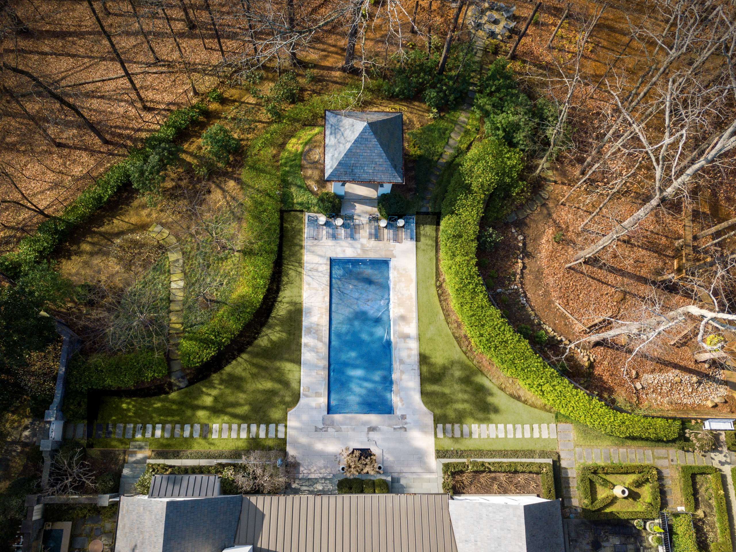 Rectangular lap pool with stone coping and pool house on wooded estate lot