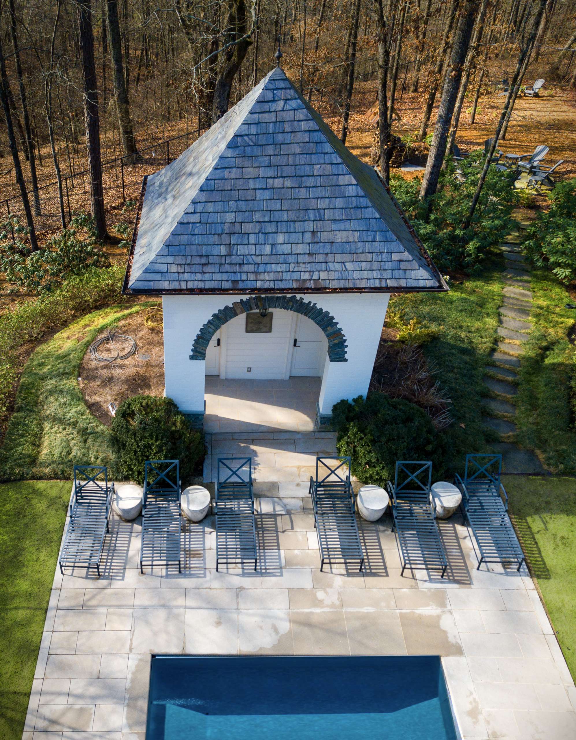 Pool house pavilion with stone deck and lounge seating on wooded property