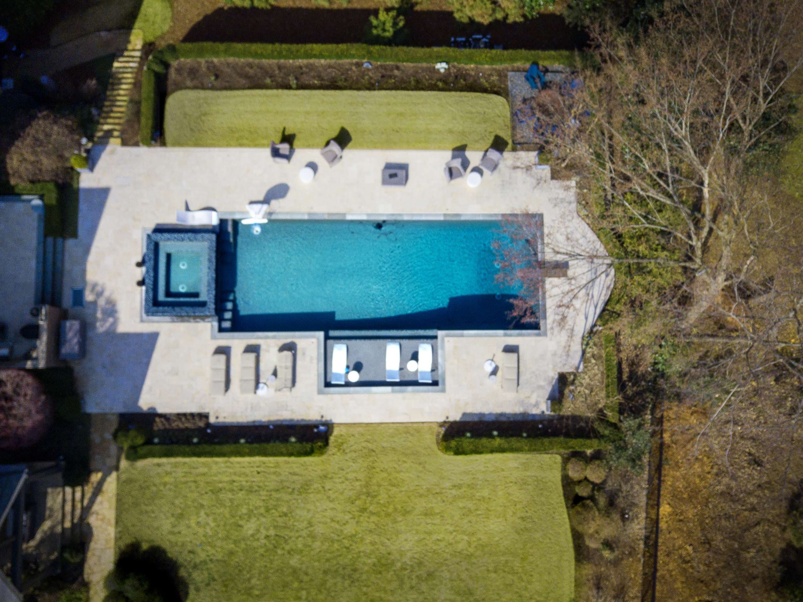 Aerial view of large pool with spa and tanning ledge on expansive concrete deck