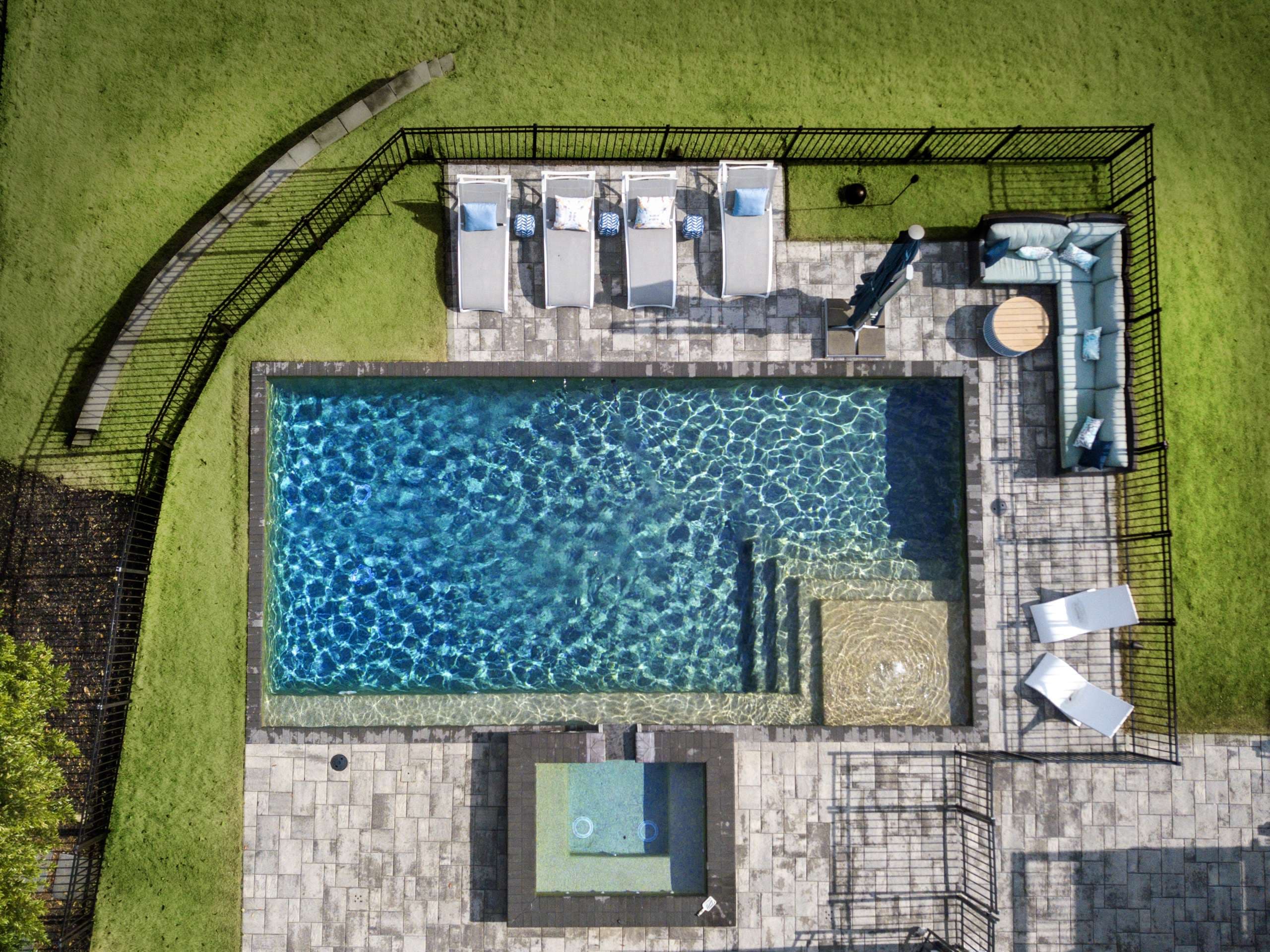Aerial view of geometric pool with tanning ledge, spa, and lounge chairs