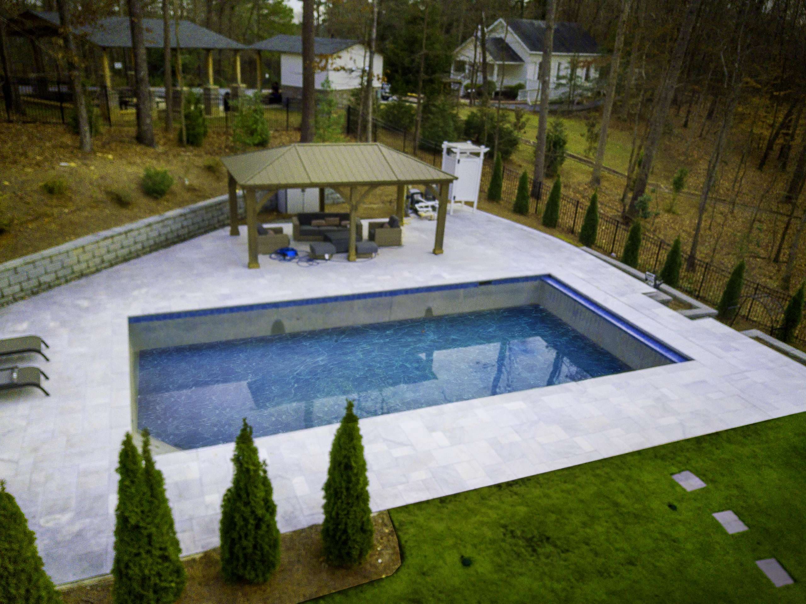 Pool renovation with large-format paver deck and pergola on wooded lot