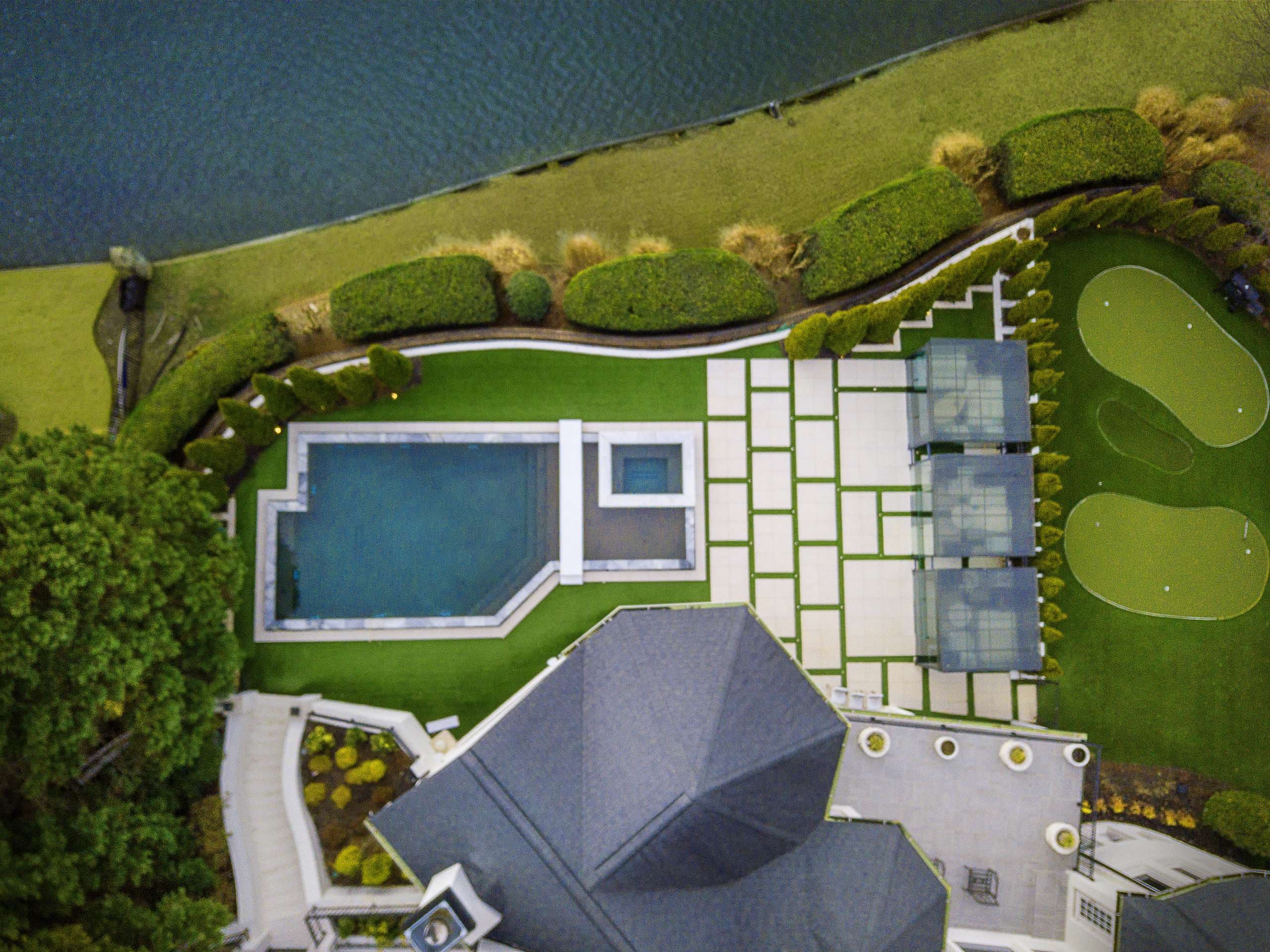 Aerial view of lakefront pool renovation with large-format paver deck and putting green